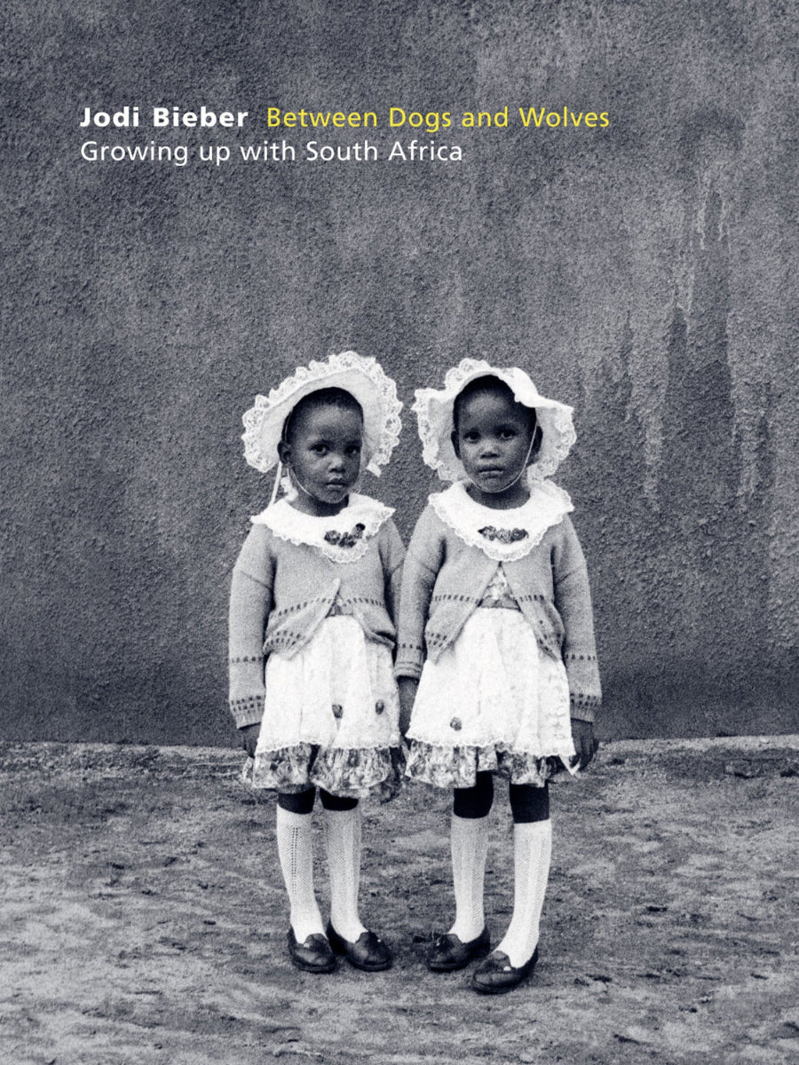 Book cover of 'Between Dogs and Wolves: Growing up with South Africa' by Jodi Bieber, featuring two children in dresses and bonnets.