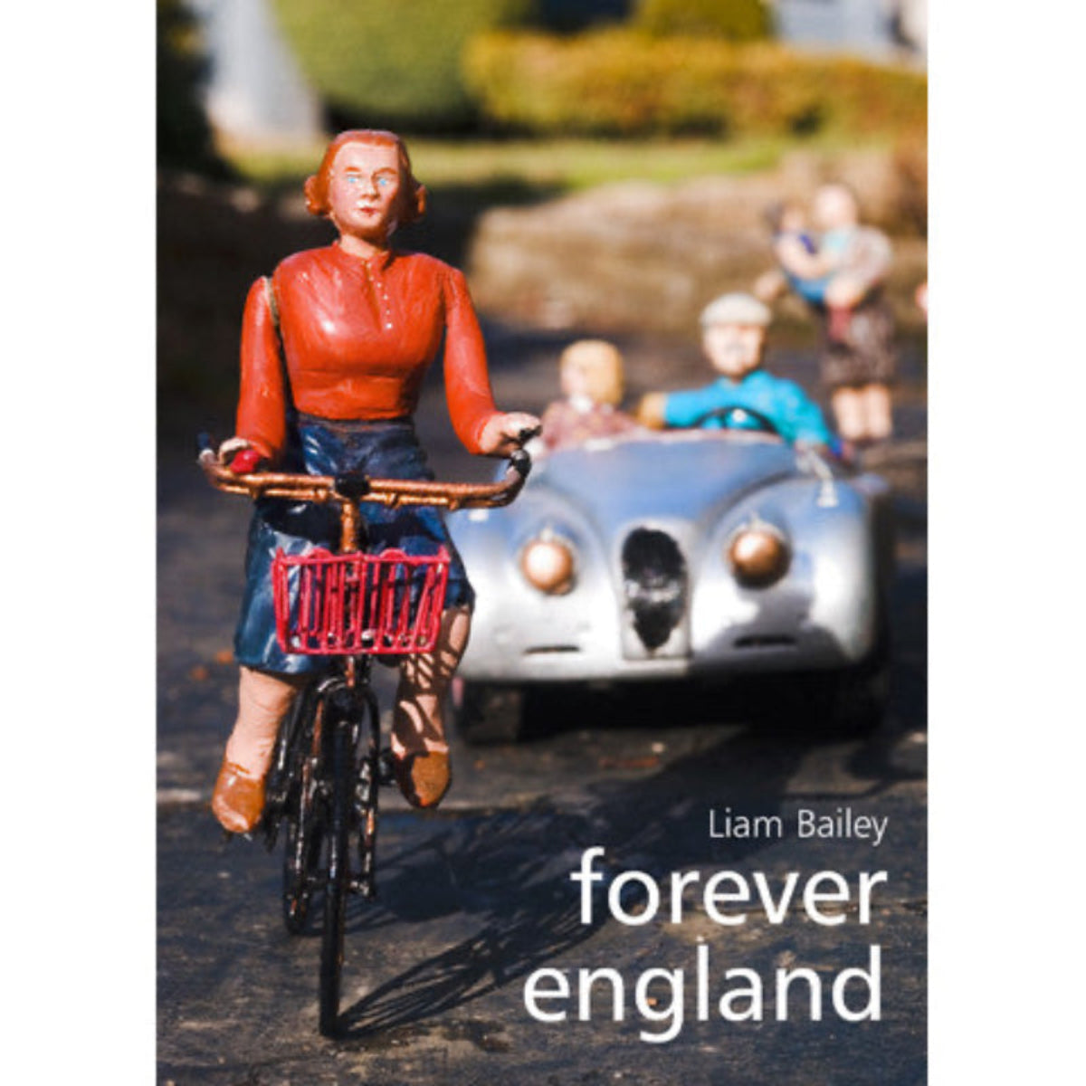 The image shows the cover of the book 'Forever England' by Liam Bailey, featuring a photograph of a figurine of a woman riding a bicycle in front of a model of a vintage car, with other miniature figures and a red brick wall in the background.